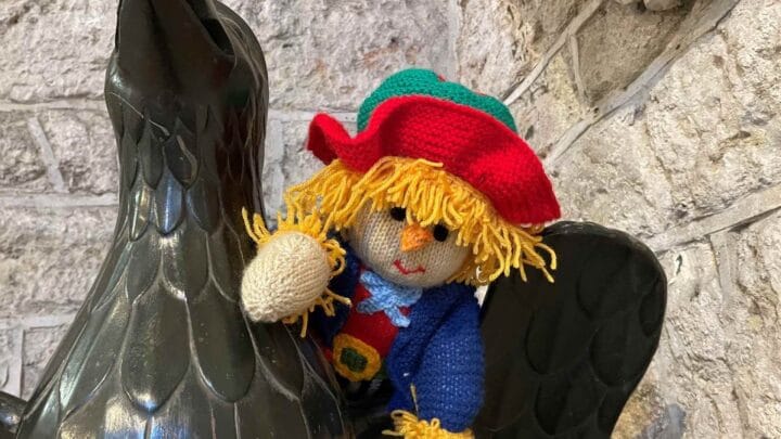 A picture of a knitted scarecrow toy, peeping out from behind the black eagle lectern in Ottery St Mary church