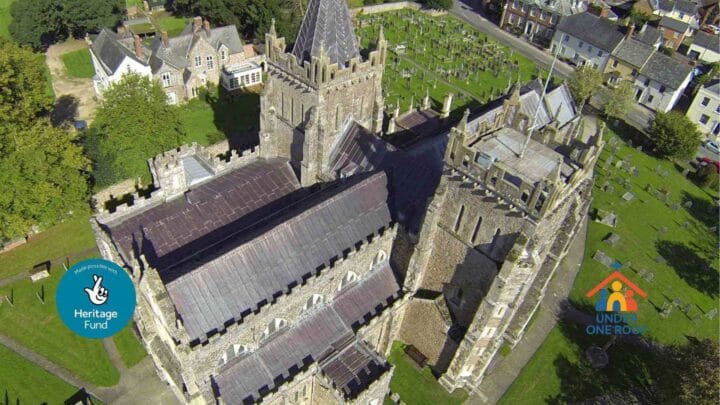 An aerial picture of Ottery Church with Under One Roof and National Heritage Lottery logos in each corner